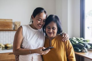 Adult woman with her arm around an older female relative looking at a smartphone