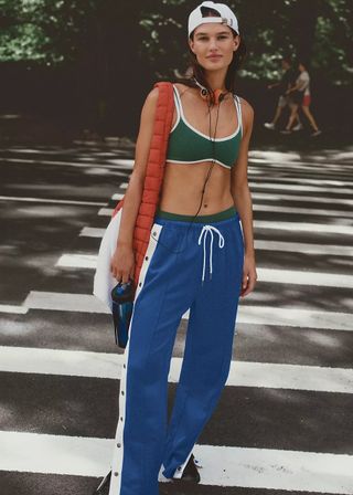 woman wearing a green sports bra and a pair of blue track pants from FP Movement