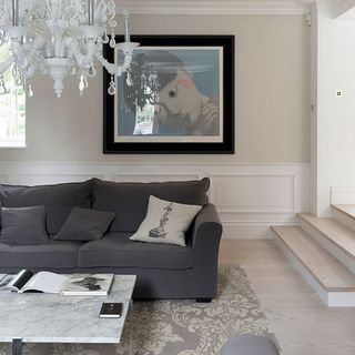 living room with white wall grey sofa with cushions chandelier cream colour flooring