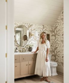 Shea McGee in a brown and cream wallpapered bathroom with wooden vanity unit and large mirror