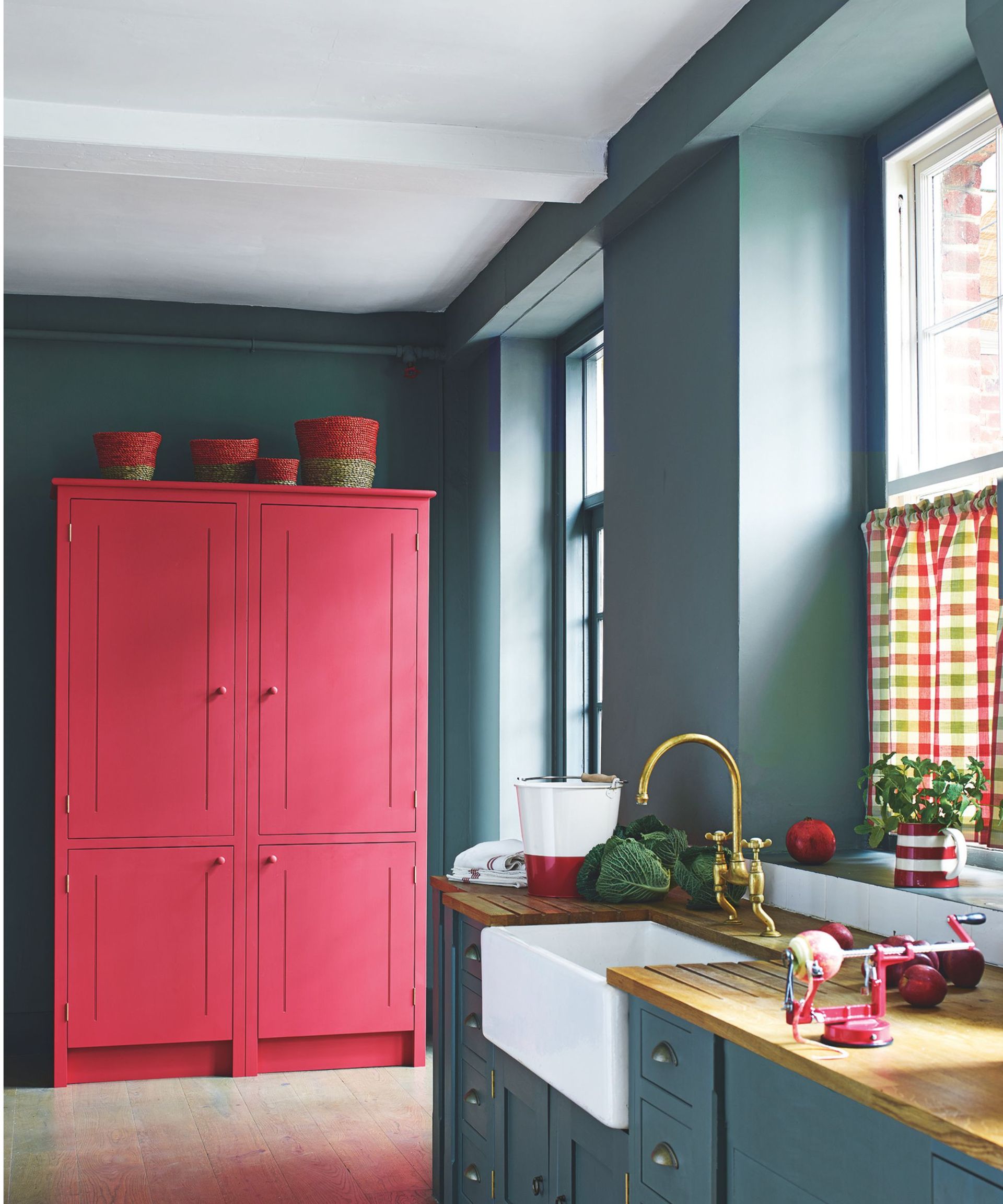 Dark blue kitchen with pink cupboard, wooden counter and gold/brass faucet above white basin.