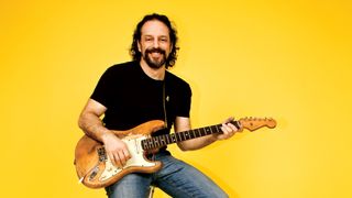 Andy Aledort holding his Fender Strat against a yellow background