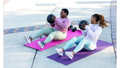 Two women performing sit-ups with medicine balls as part of an abs workout