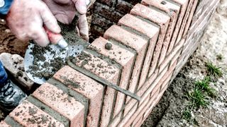 Hands using a brick jointer finishing a red brick garden wall