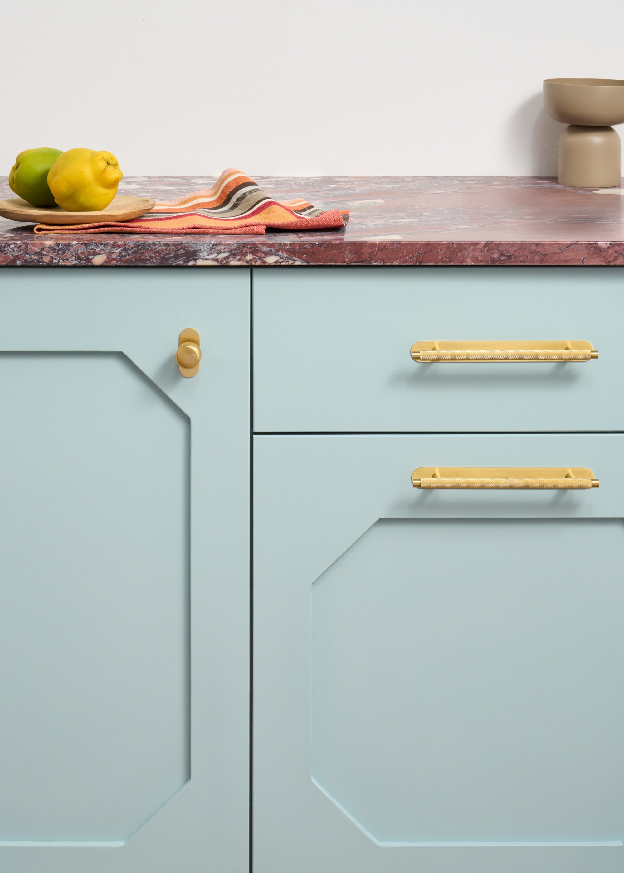 A pale blue kitchen close up of cabinetry and brass handles