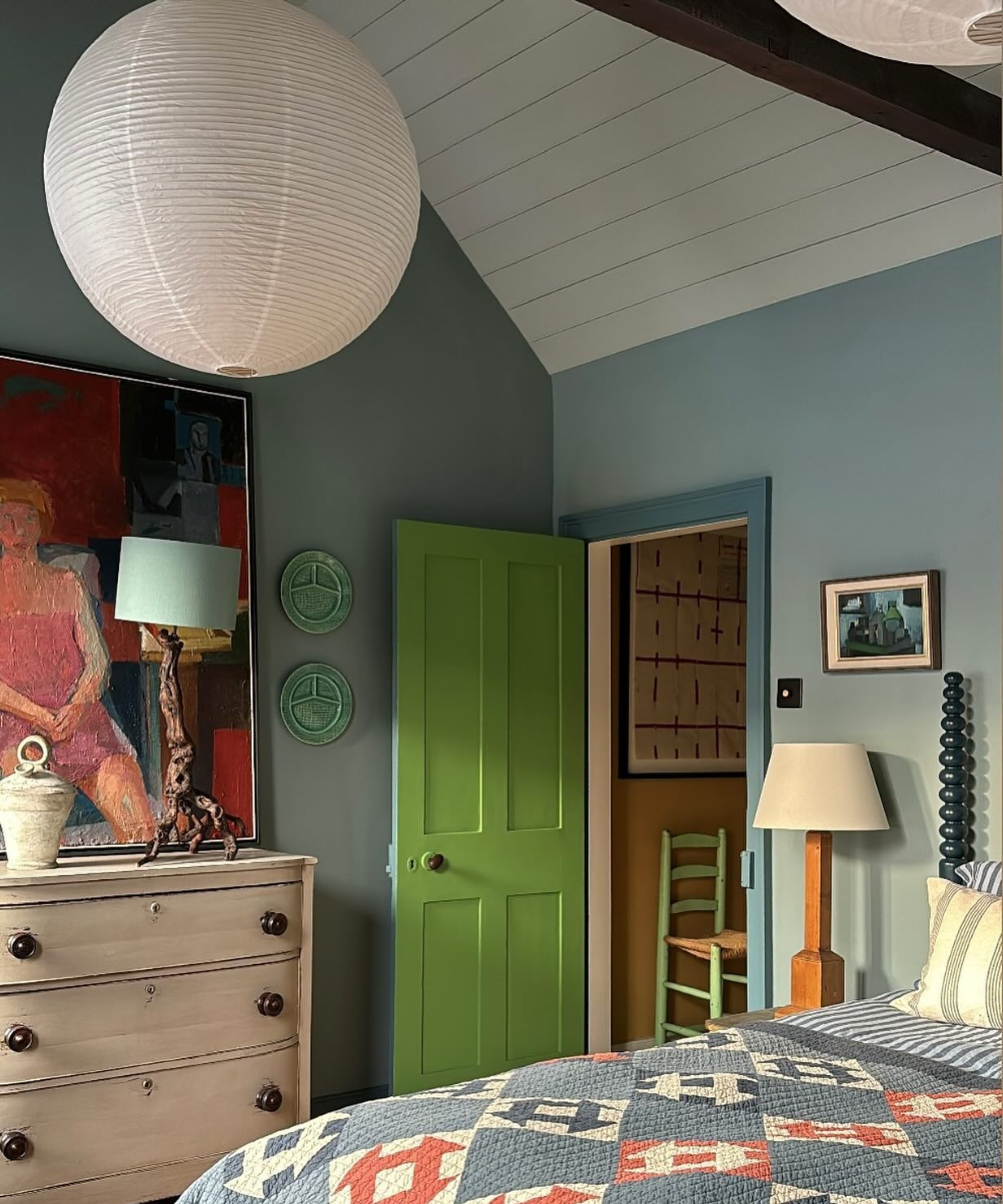 a bedroom with a quilt on the bed, a white dresser, blue painted walls, and a green door