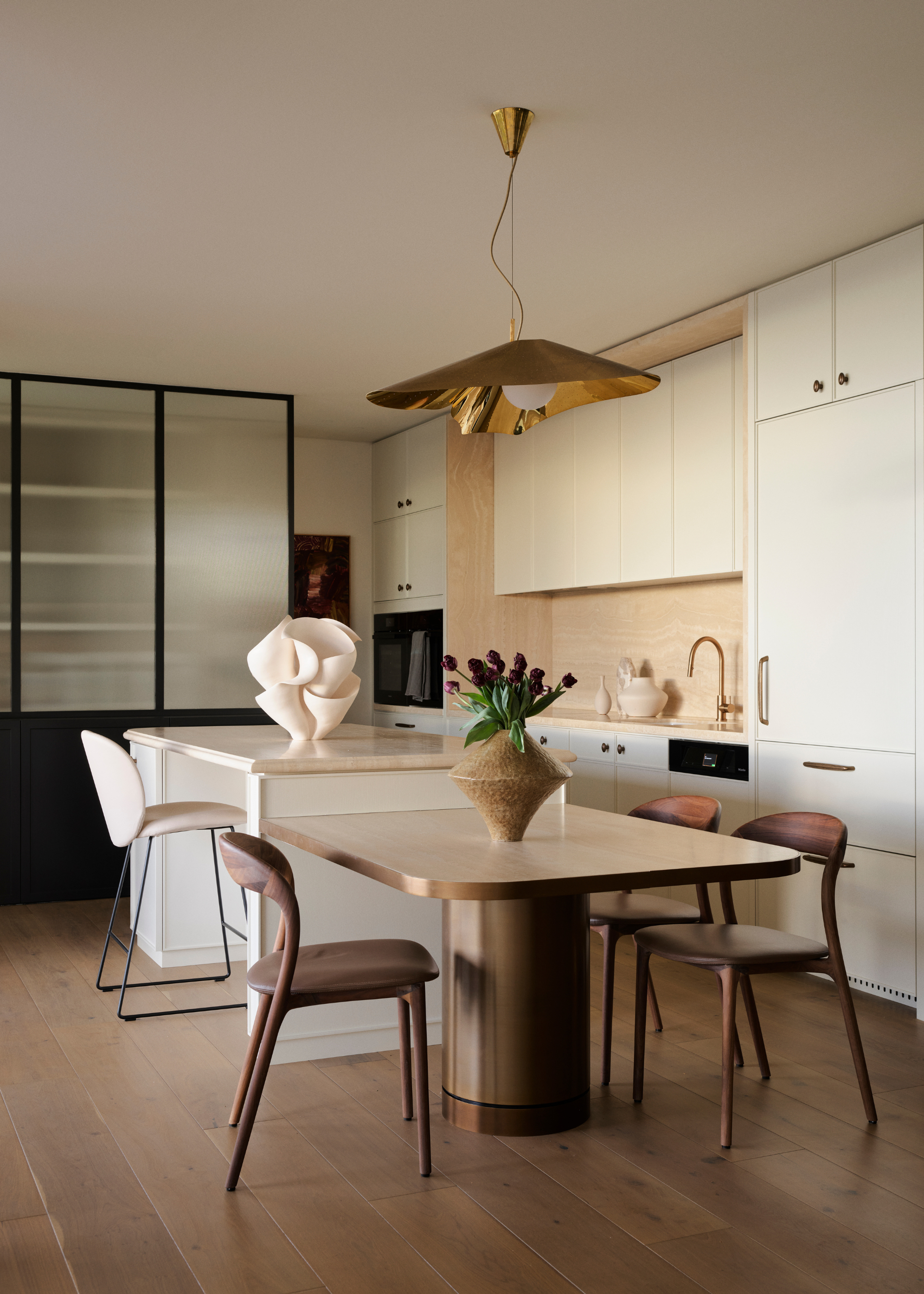 A dining room near an open concept kitchen with gold pendant lighting and a vase with flowers