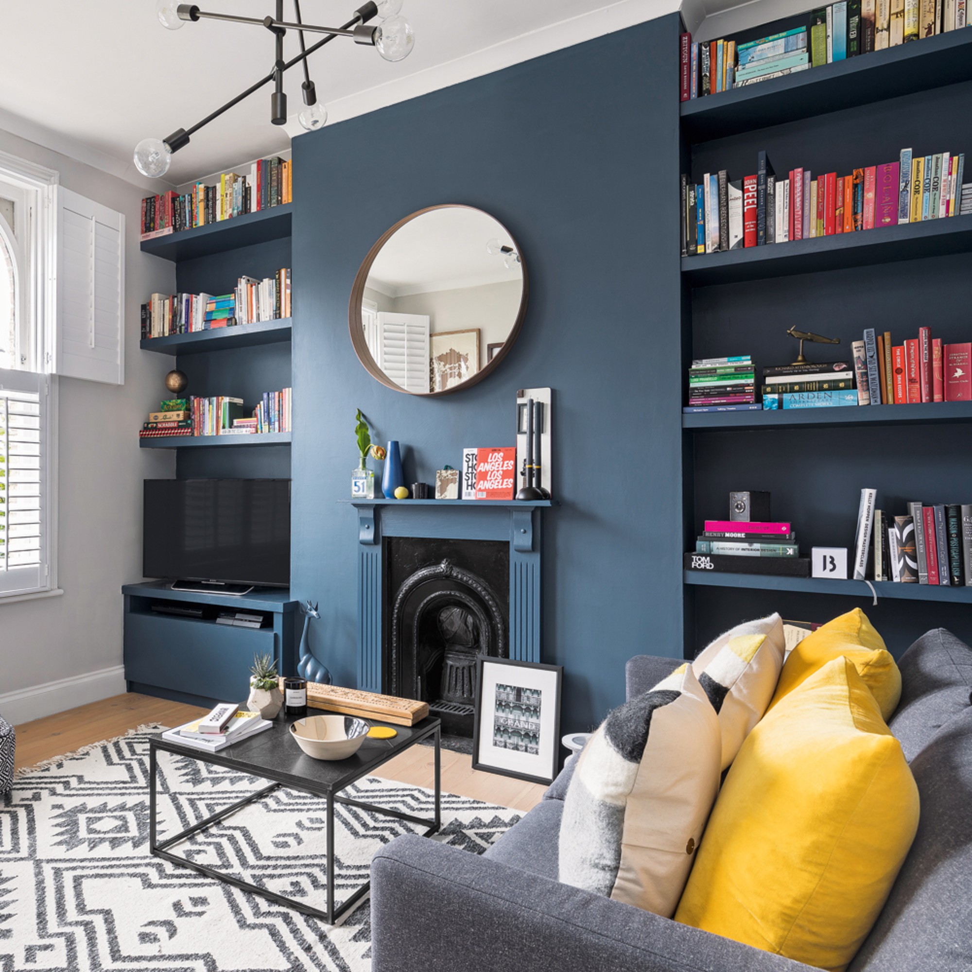 A living room with a navy feature wall with a fireplace, alcoves and a TV in one of them