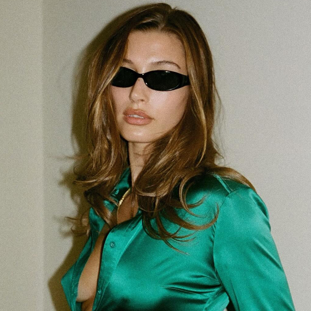 Hailey Bieber wearing a green shirt and sunglasses with muted brown hair