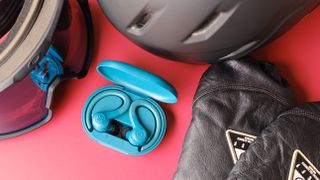 JLab Go Air Sport earbuds next to snowboard gear on a red table.