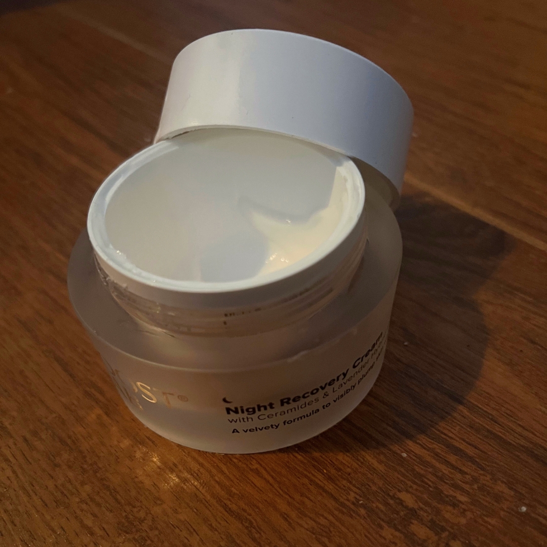 Empty and open white tub of Boost Lab Night Recovery Cream with dark wood background