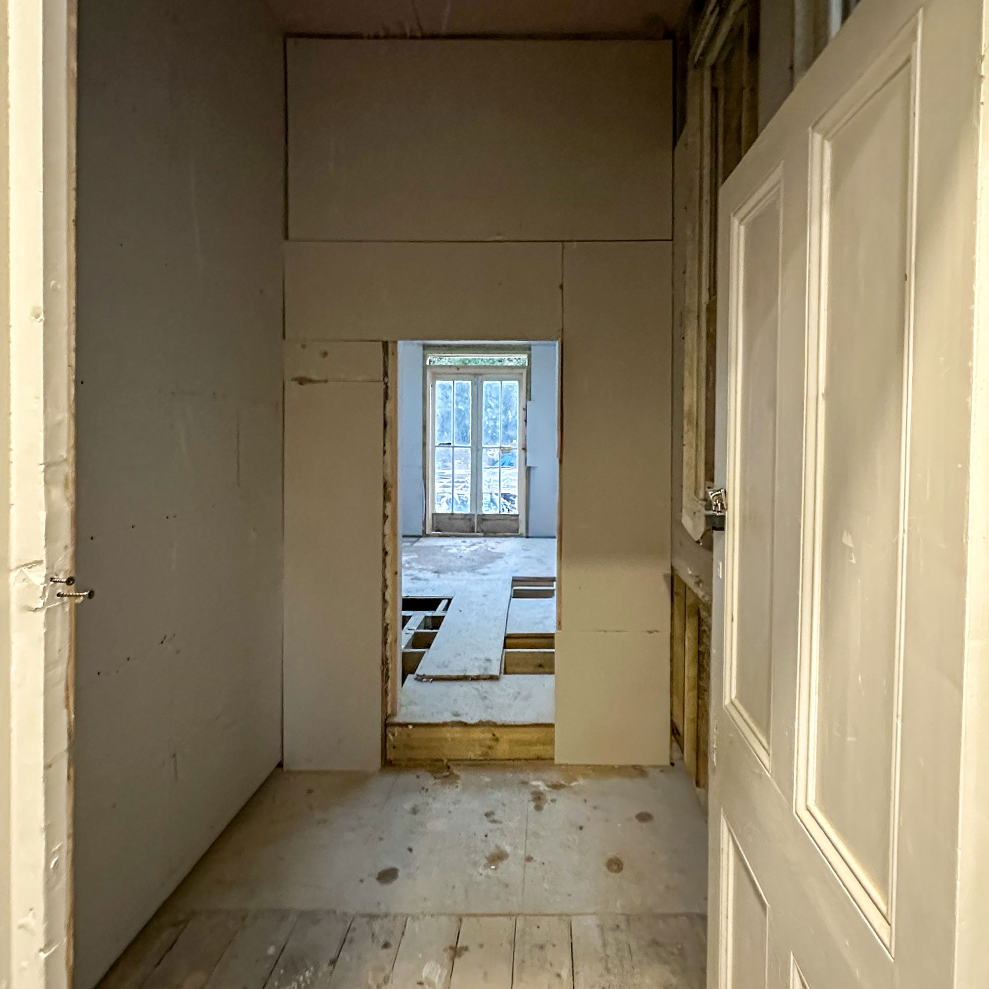 View of hallway into room, mid-renovation, with bare walls and floorboards