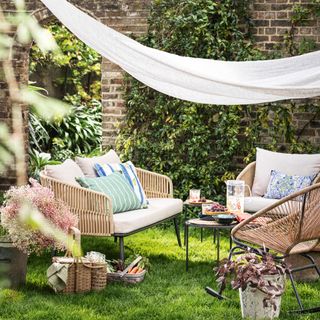 a lush lawn with garden furniture set up in a circle and a makeshift shade sail overhead