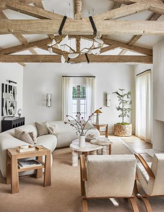 A neutral living room with wood beams on the ceiling and white seatinh