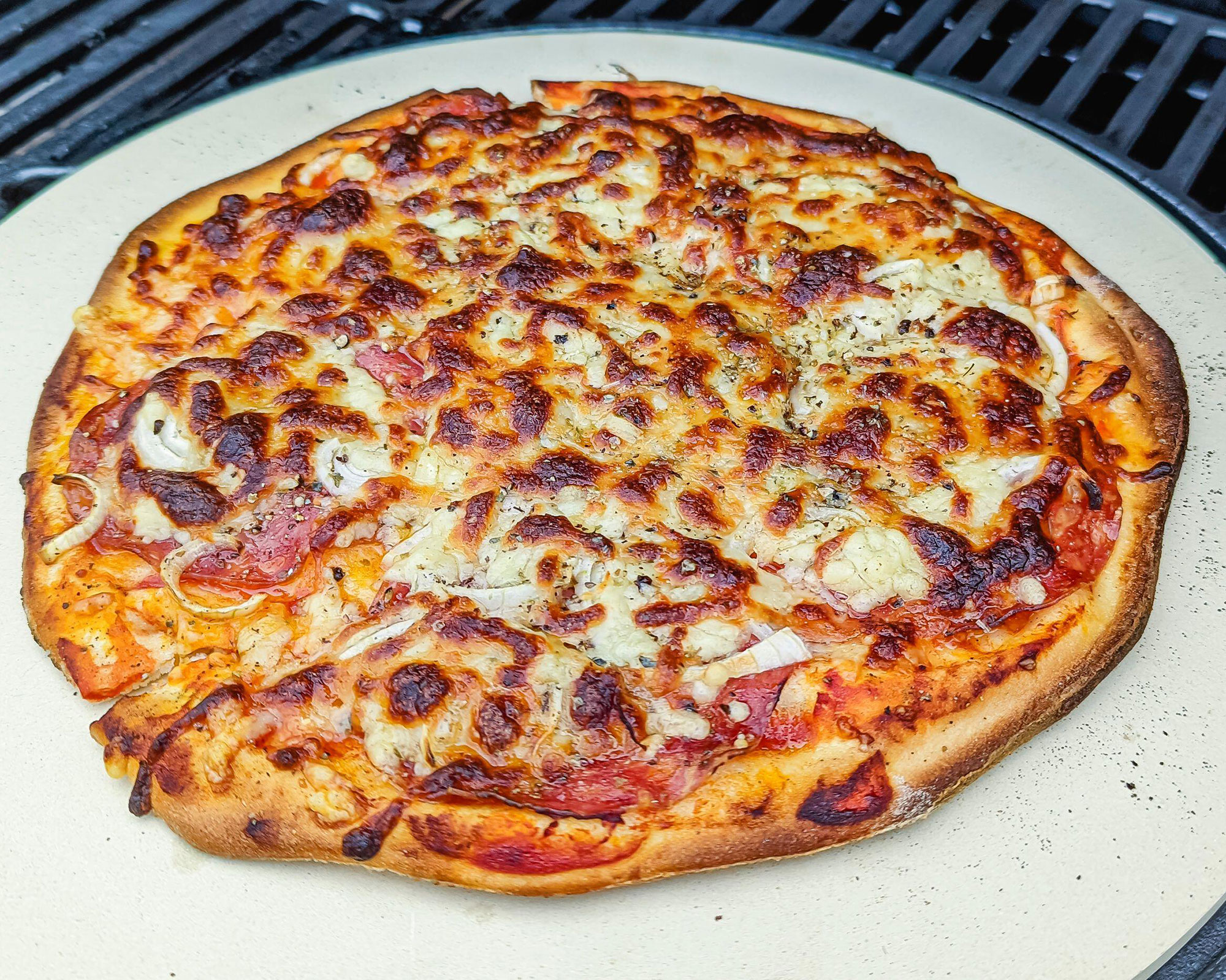 pizza cooking on a pizza stone over an outdoor grill