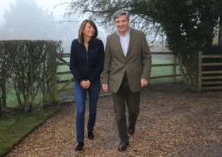 Carole Middleton wearing jeans and a dark sweater walking outside in front of a fence next to her husband Michael Middleton