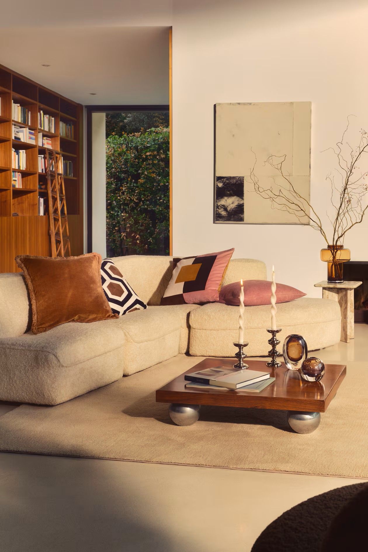 Image of a modern living room with a 70s aesthetic. There is a curved boucle sofa with multicolored pillows and a wooden and chrome coffee table in the center of the room.