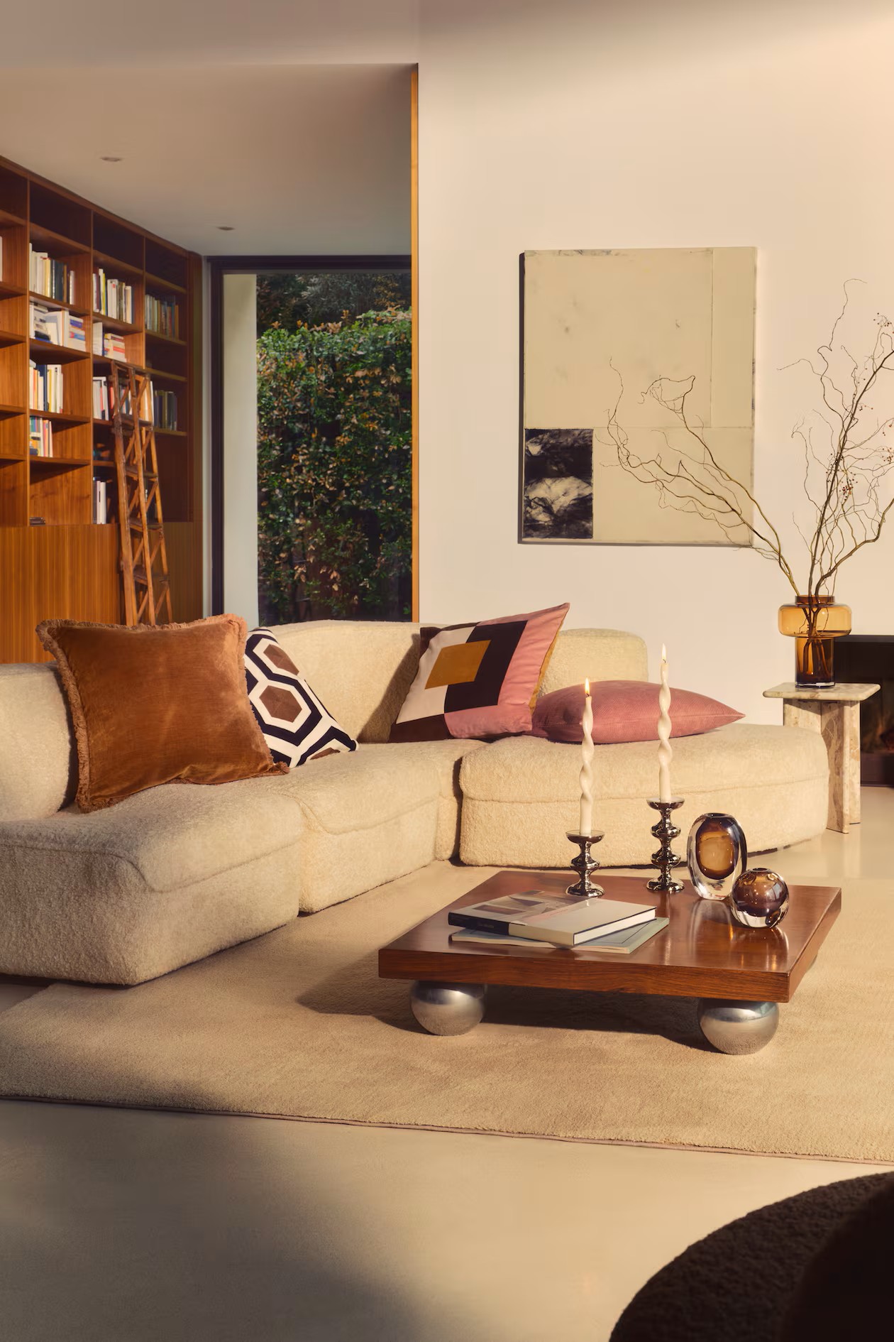 Image of a modern living room with a 70s aesthetic. There is a curved boucle sofa with multicolored pillows and a wooden and chrome coffee table in the center of the room.