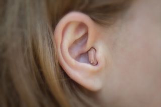 A woman is wearing a completely-in-the-canal hearing aid.