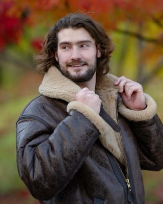 Portrait of man wearing flight jacket standing in front of floral background