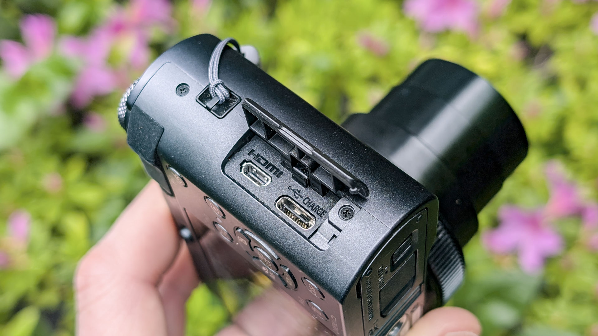 Close up of the Panasonic Lumix TZ300 compact camera's connection ports, with a colorful floral backdrop, view of the top and the lens is extended