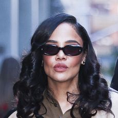 Tessa Thompson wearing a leather jacket, brown polo shirt, gray column skirt, and pumps