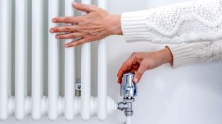 Hands touching a white column radiator, against a white wall, and thermostatic radiator valve