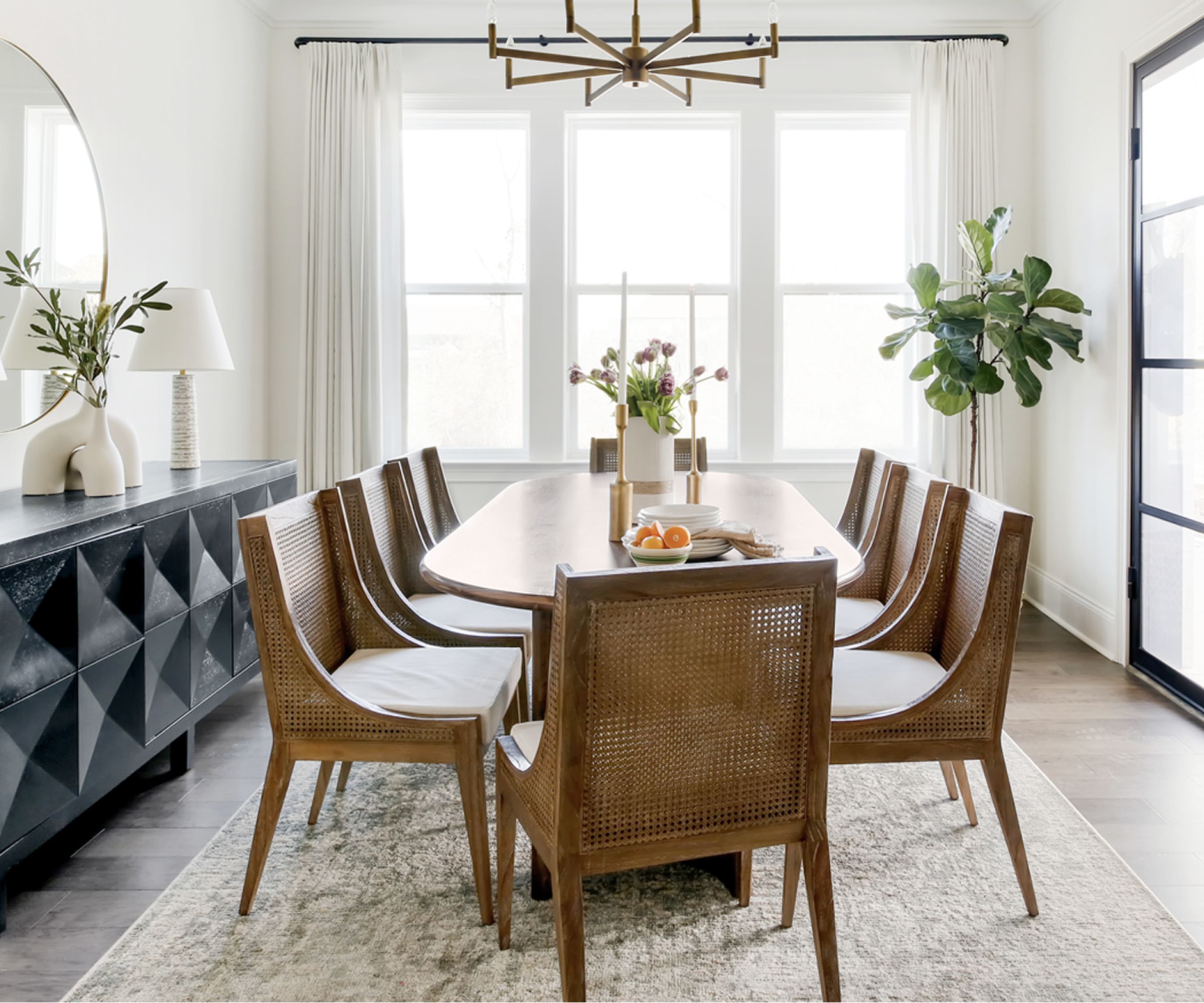 A white dining room with an oval wooden table and a black sideboard