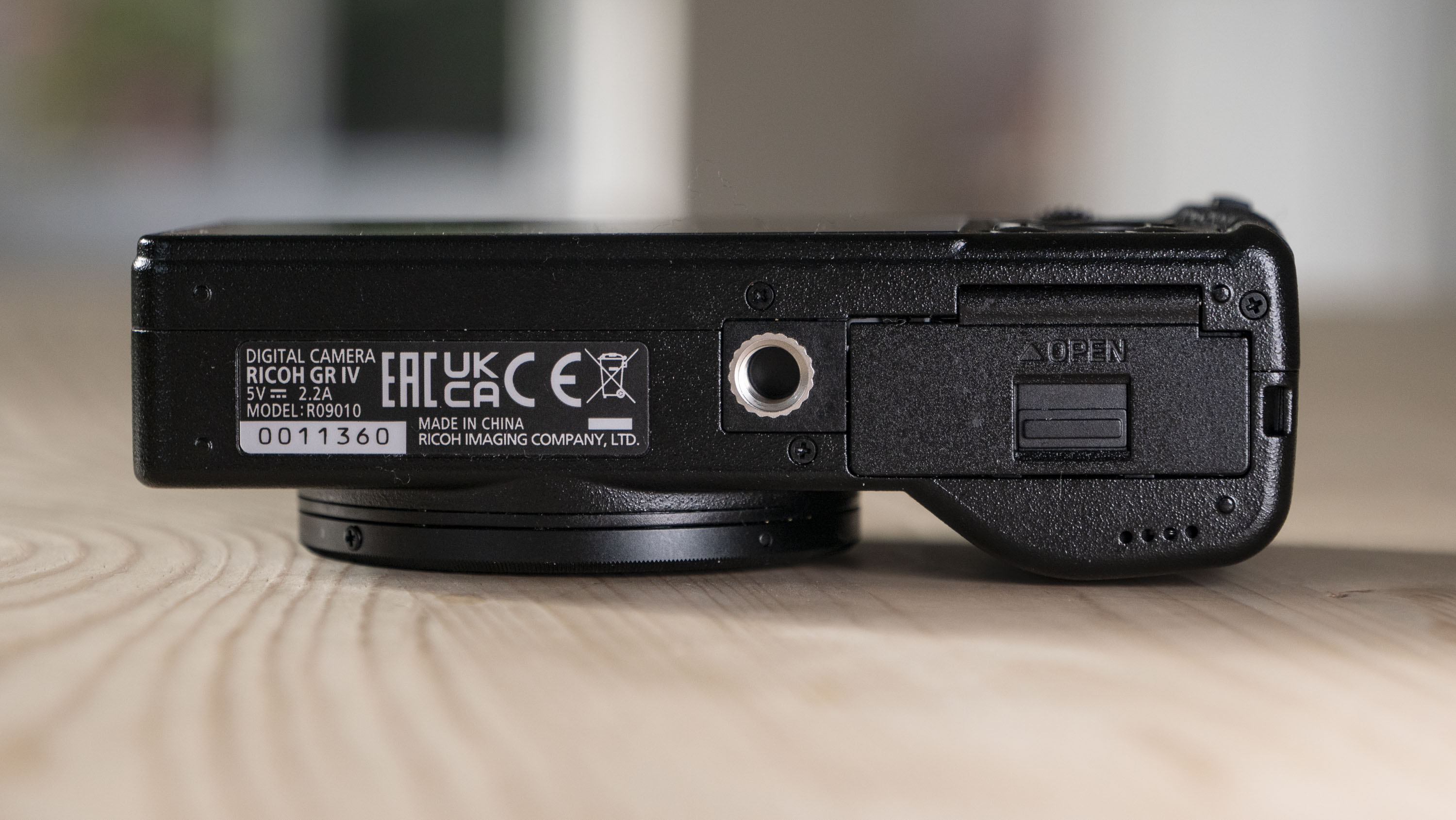Underside of the Ricoh GR IV compact camera, on a wooden table