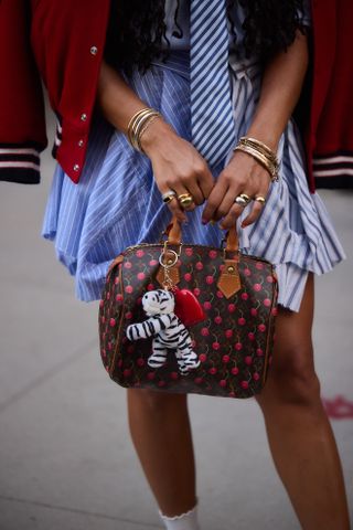 a woman at new york fashion week carries a louis vuitton cherry print bag with a tiger charm attached to the front