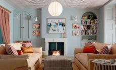 Light blue living room with beige striped ceiling, black and white striped ottoman, beige sofas and artwork