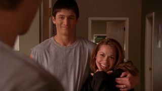 Nathan with his arm around Haley who is smiling while holding her chin with one hand in One Tree Hill.