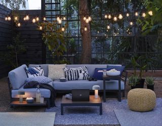 Modern garden ideas: outdoor sofa, rug and coffee table with string lights and lanterns