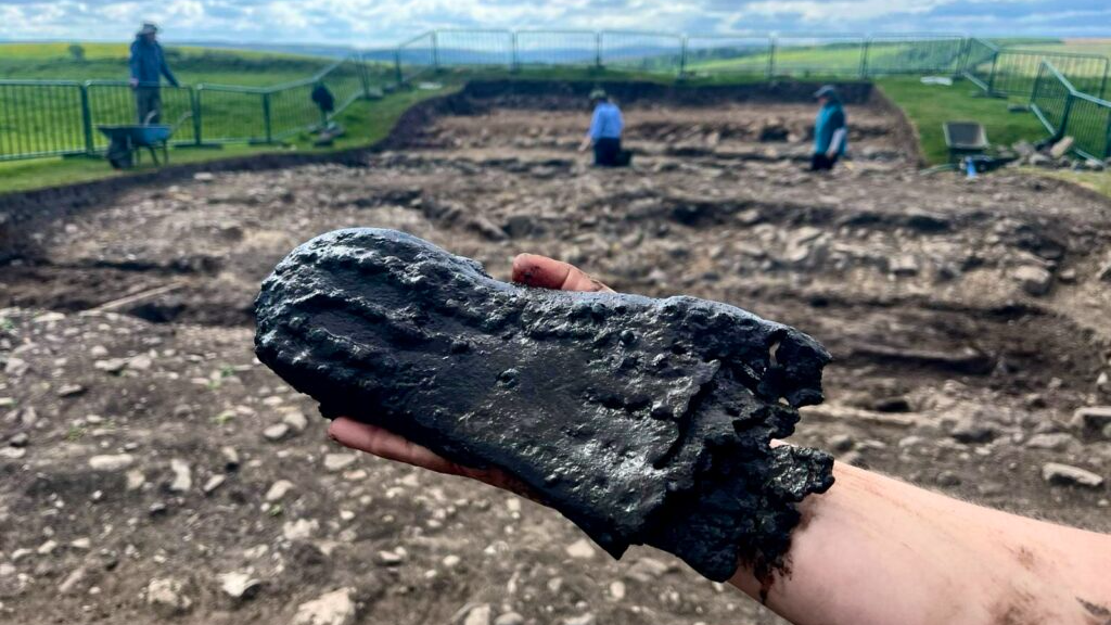 A person holds a leather shoe sole, black from centuries in the water, with hobnails on the bottom