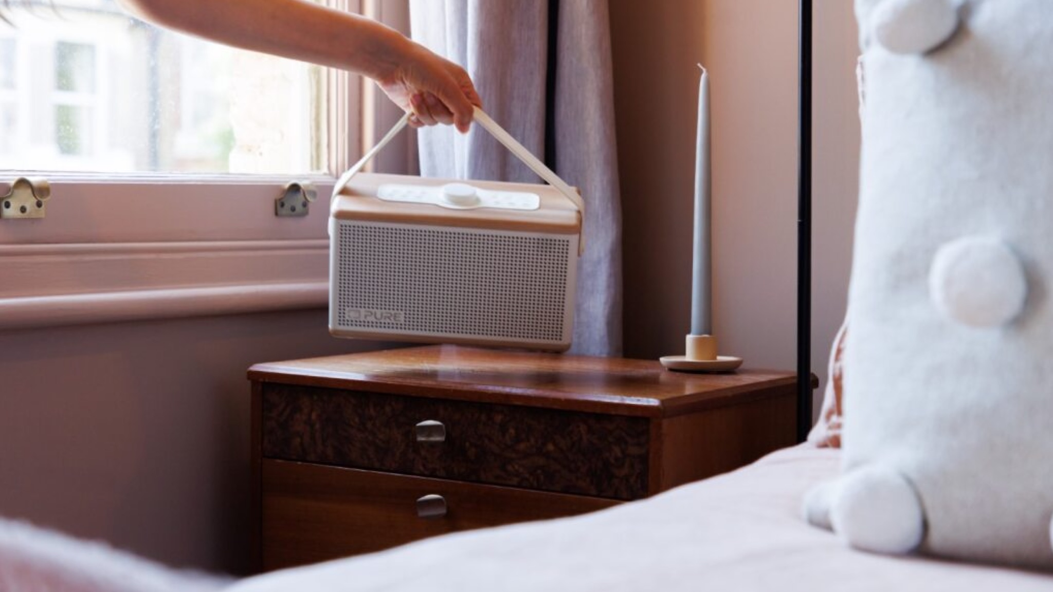 A Pure Aura Bluetooth speaker being placed on a bedside table in a bright room
