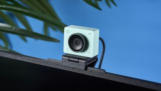 a photograph of a 1 inch wide mint webcam with a 4K sensor and built-in microphone, photographed against a blue background