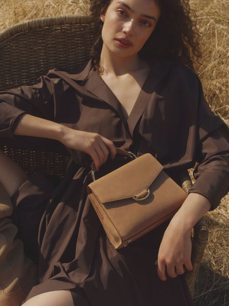 Woman in brown dress in a field with a bag