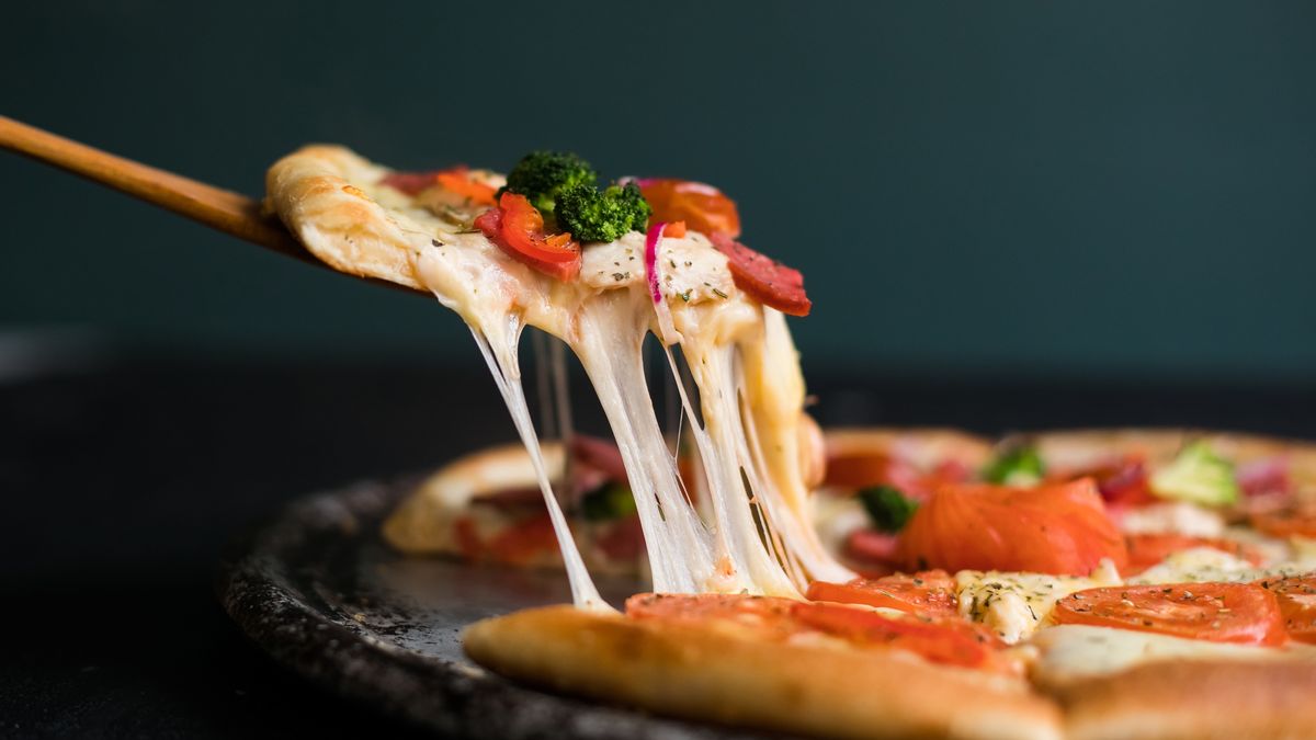 A slice of pizza being removed from the pie with stringy cheese