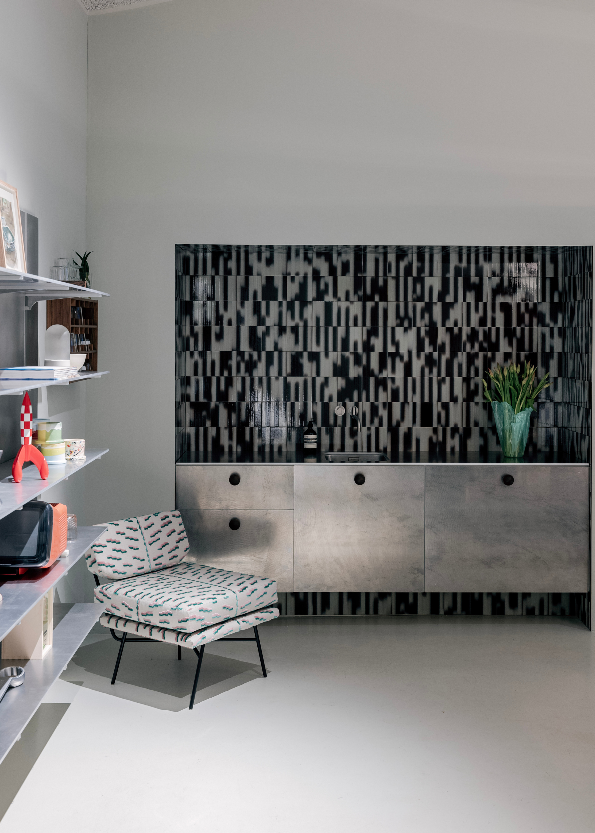 a small living area with a sanded steel cabinet with palet black and white tiles behind