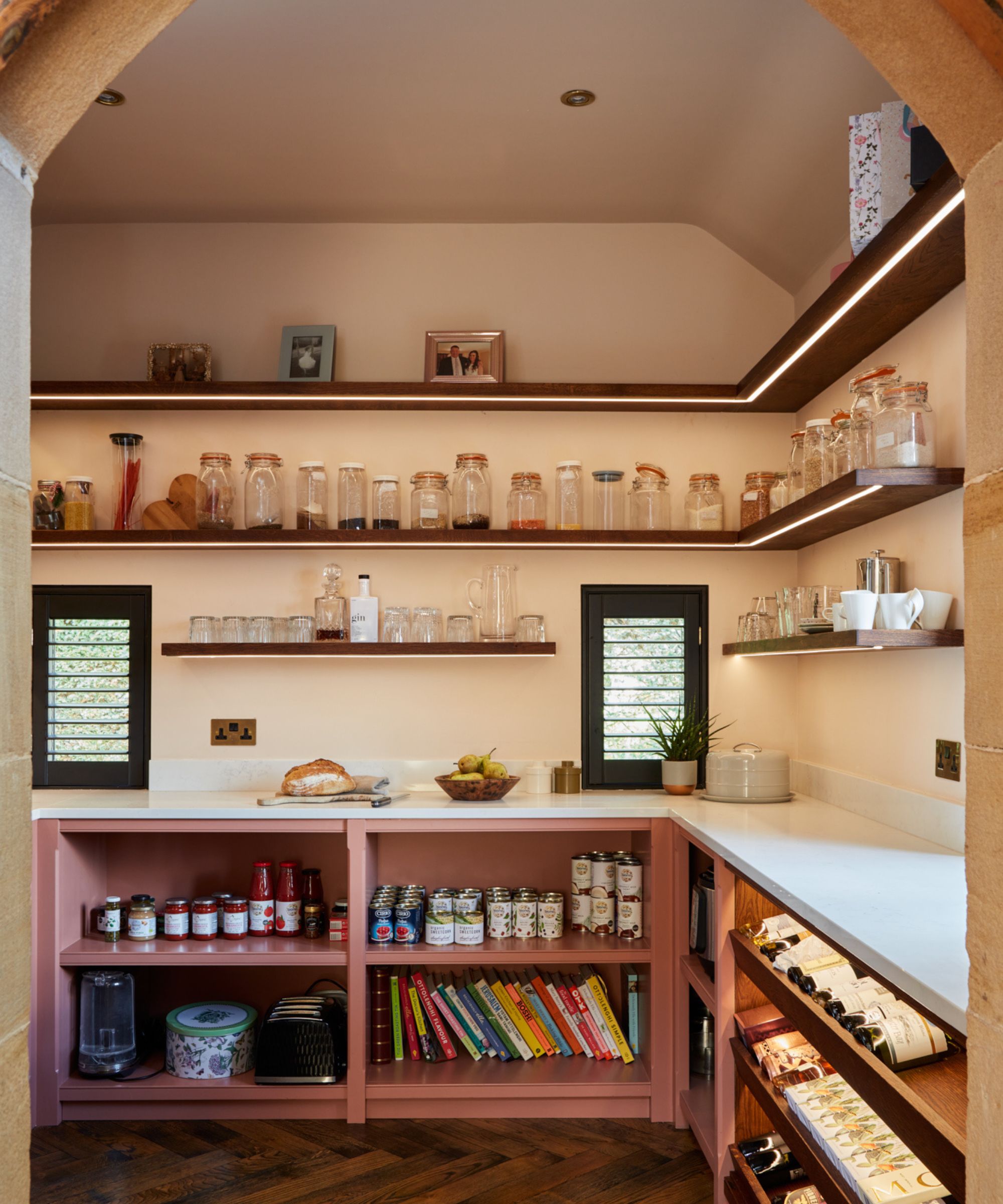 A beautifully organised walk-in pantry with open shelving, soft pink cabinetry and integrated lighting, designed for both storage and display.