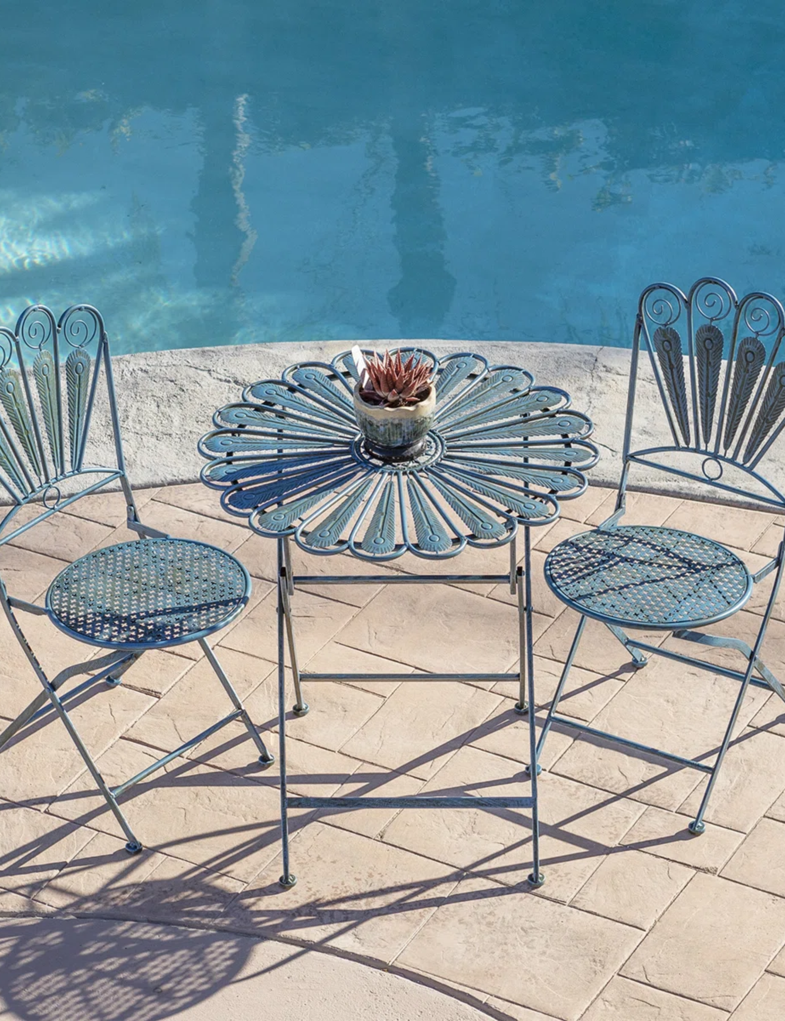 Whimsical outdoor iron bistro set in peacock blue sitting poolside