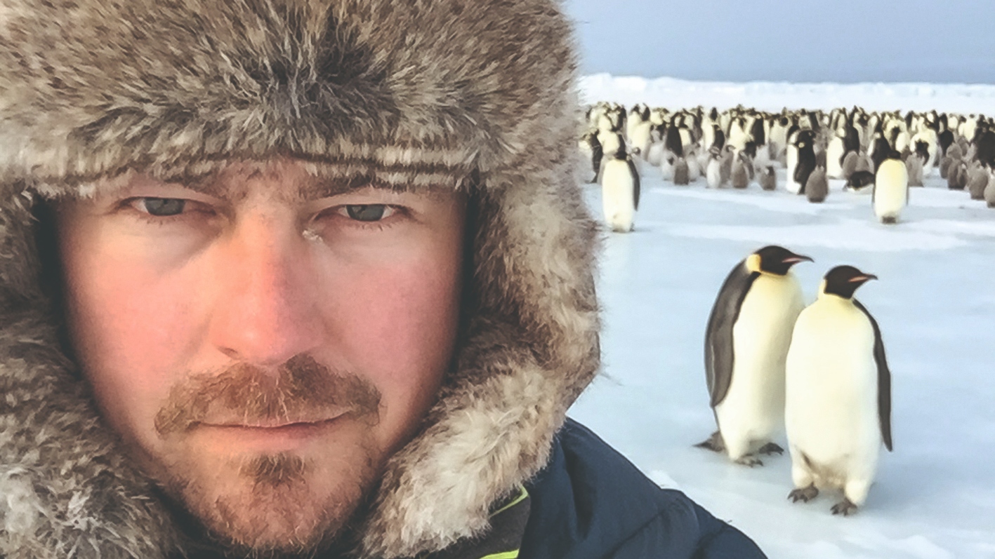 Jeff Wilson in a fur hat with penguins behind him