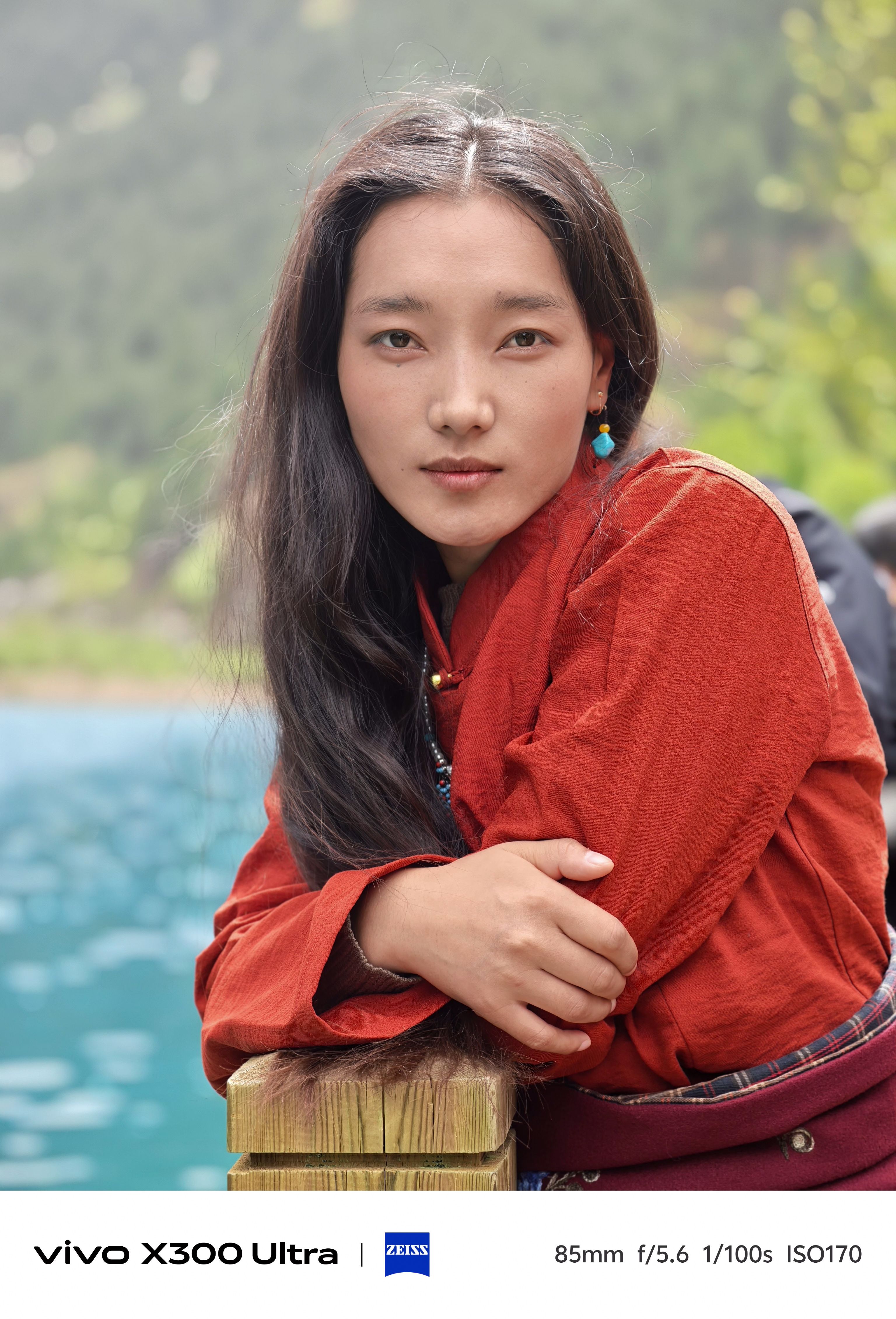 A portrait of a woman leaning against a wooden railing, looking directly forward with a calm expression.