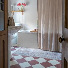 Small neutral bathroom with red and white vinyl checkerboard floor tiles and a soft pink shower curtain