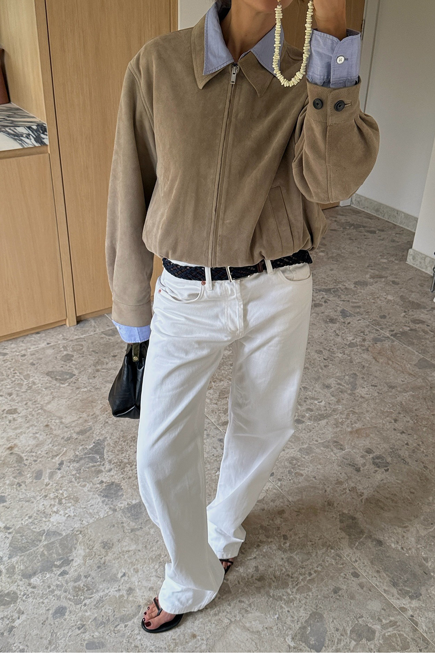 A woman wearing a tan suede jacket, white jeans and black flip flops