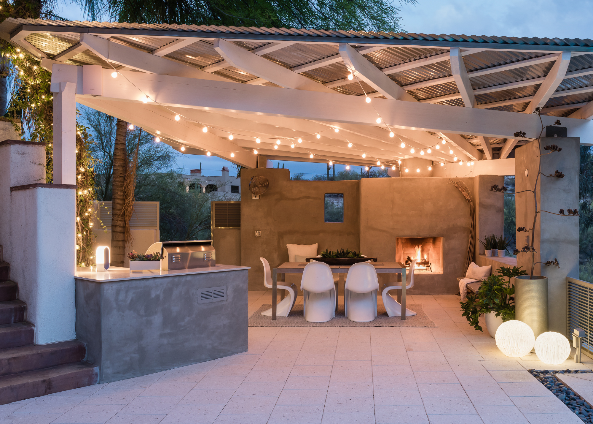 an outdoor kitchen under a canopy with a fireplace and a dining area and lots of outdoor lighting