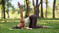 woman in park does a thread the needle yoga pose on the grass