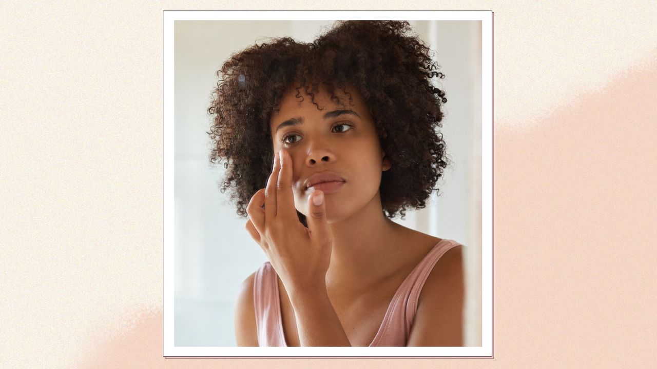 A close up of a woman with curly hair applying skincare to her cheek whilst looking in the mirror/ in a cream and beige template