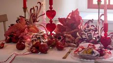 Festive Valentine's Day tablescape decorated with heart motif linens, dried florals, and pink-and-red ornately detailed glassware.