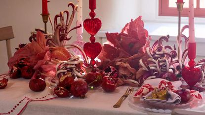 Festive Valentine's Day tablescape decorated with heart motif linens, dried florals, and pink-and-red ornately detailed glassware.